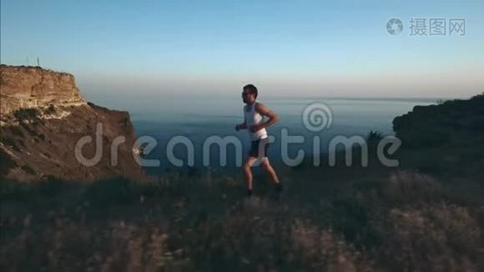 运动帅哥正在用电话和耳机做运动，日落时沿着海边跑步，然后慢跑视频
