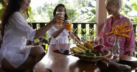 在热带森林的夏季露台上，年轻女孩会在早餐时一起品尝带果汁的玻璃杯，美女们视频
