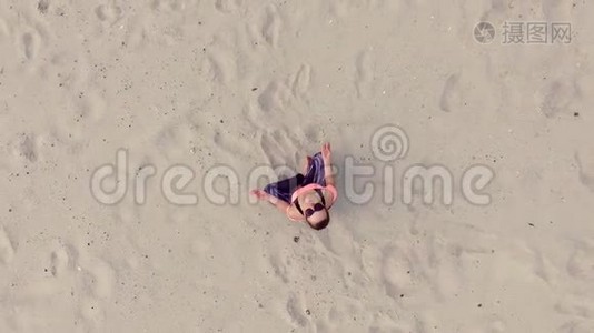 时尚的年轻美女戴着太阳镜，坐在沙滩上摆出莲花的姿势，冥想，在一个视频