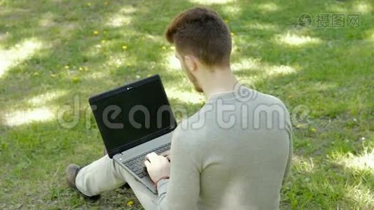 年轻人坐在公园的草地上，在笔记本电脑上贴着胶带视频