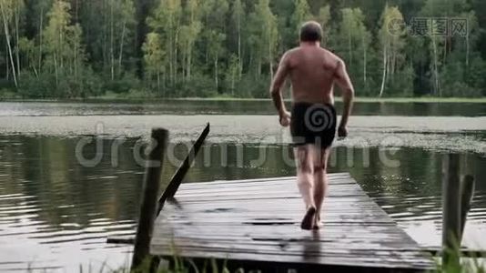 白种人成熟的男人从湖边的木墩上跳下来。视频