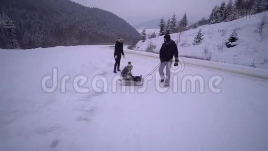 年轻的幸福家庭在雪林里玩得很开心。 父母把他们的小儿子卷在雪橇上。 晚上散步。视频