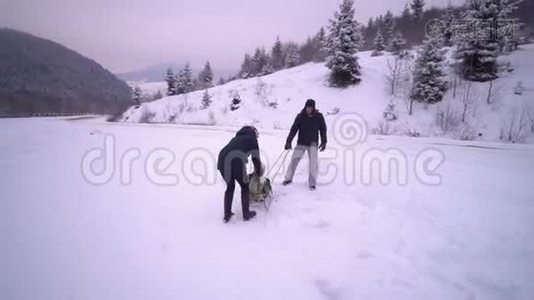 年轻的幸福家庭在雪林里玩得很开心。 父母把他们的小儿子卷在雪橇上。 晚上散步。视频