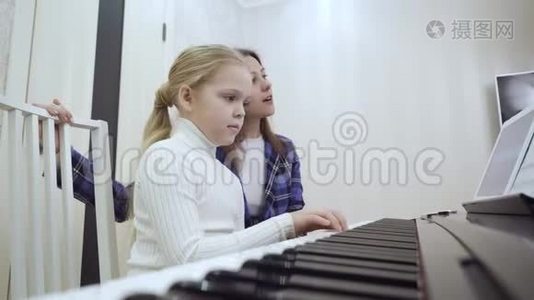 年轻的老师和小可爱的女孩在电动钢琴上演奏。视频
