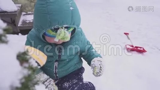 男孩，孩子躺在圣诞树附近的雪上，在户外玩装饰。视频