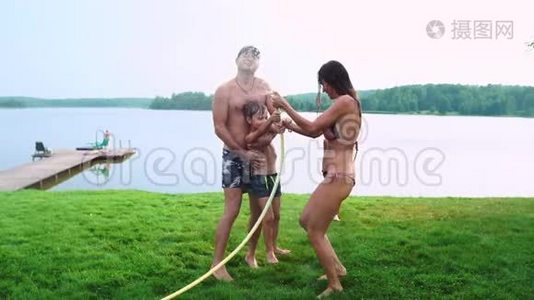 爸爸妈妈和两个儿子在夏天的草地上为草坪浇了一根水管。 在湖边的乡村别墅视频
