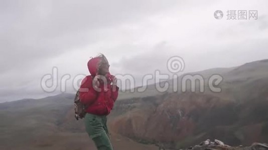 年轻的女游客在大雨下在山上散步。 一个背着背包的女孩旅行者视频