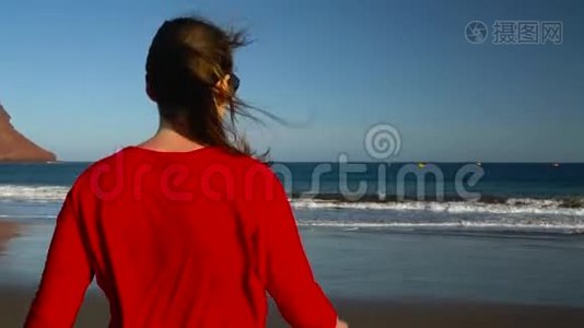 幸福的年轻女子穿着红色的连衣裙，在日落时步行到海边的水上。 无忧无虑的现代生活理念视频