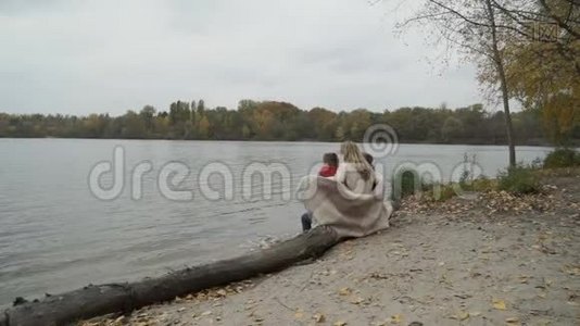母亲和儿子坐在河边的一根木头上，一家人欣赏秋天的景色视频