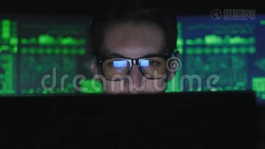 戴眼镜的黑客程序员正在电脑上工作，在电脑安全中心喝着咖啡，里面摆满了显示器视频
