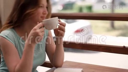 一个穿蓝色连衣裙的女孩正在夏天的咖啡馆里喝咖啡。视频