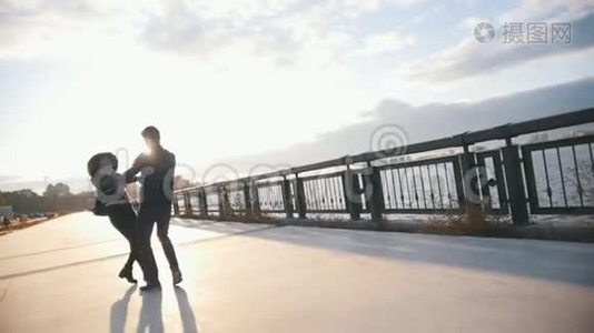 城市长廊上的年轻一对，日落时男人拥抱和旋转女朋友，慢镜头视频
