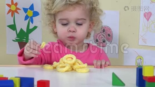可爱的脸蛋女孩吃玉米圈，坐在她的桌子旁边，玩具和图纸视频