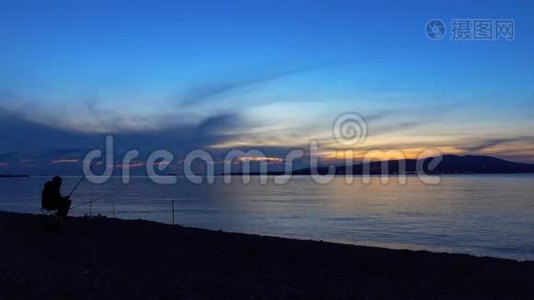 海岸上的渔夫坐着钓到一条鱼。 四周风景优美。视频