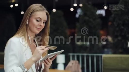 微笑的年轻女性从金色信用卡上获取了一个与平板电脑一起工作的数据视频