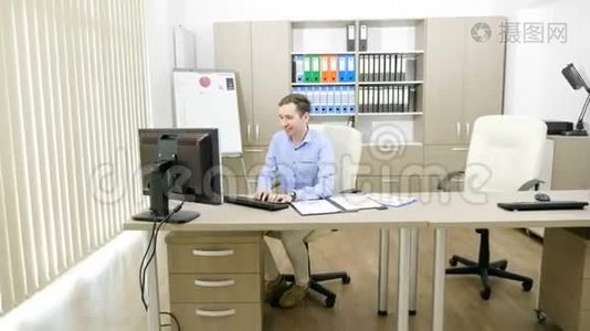 一位雄心勃勃的年轻商人正在他的办公室里工作，电脑旁边放着装满图表的文件夹视频