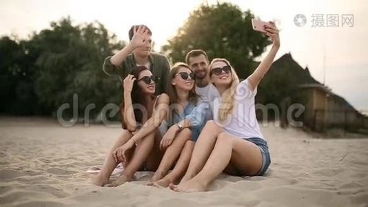 拍摄一群年轻朋友在海滩上自拍。 男人和女人坐在温暖的沙滩上拍照视频