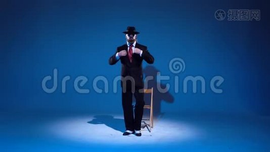 戴着黑帽子的优雅男人正在跳舞。在蓝色背景上聚光灯。视频
