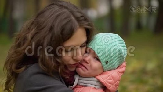 一幅美丽的年轻女子和一个哭泣的孩子在秋天公园的肖像。 小女孩在哭。 年轻的母亲安慰她视频