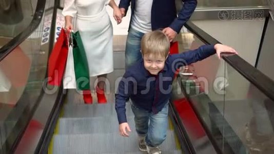 家庭圣诞购物。 带着孩子的父母带着礼物包上扶梯。 大型多色包装视频