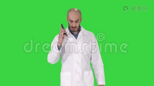 专业医生在绿色屏幕上行走时用手机交谈，Chroma键。视频
