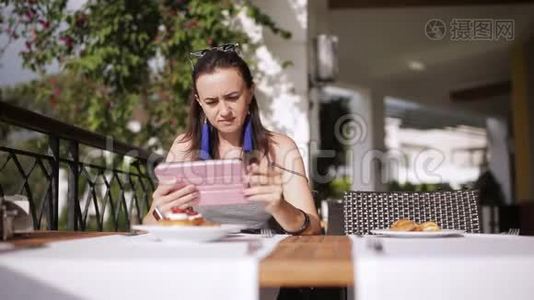 女孩在小酒馆里吃早餐，在街头餐馆里用平板电脑浏览互联网视频