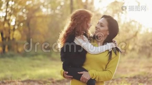 一位美丽的妈妈和她可爱的女儿正在秋天的公园里散步。 妈妈把女儿抱在怀里。 他们视频