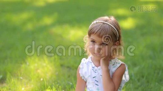 绿色草地背景下公园可爱的微笑小女孩的肖像。视频