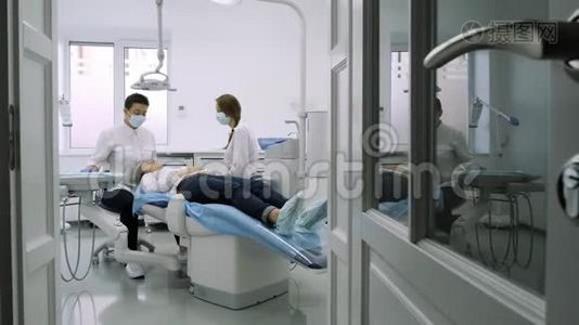 病人坐在蓝色的牙医椅上，牙医助理帮助他。视频
