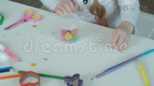 一个快乐的小女孩从一个容器里拿出五颜六色的塑料，桌面上摆着数字和彩色铅笔视频
