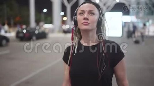 年轻迷人的时髦女性使用智能手机，晚上在街上听音乐跳舞视频