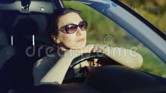 一个戴太阳镜的女人在车里放松。 坐在车轮后面，欣赏日落时的美景。 快乐的司机视频