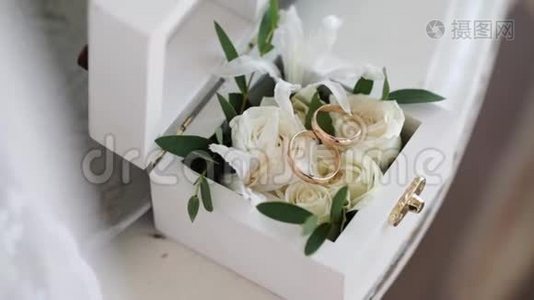 两个金色结婚戒指放在一个白色的木箱里，里面放着玫瑰花视频