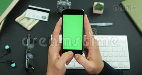 男人拿着一个绿色屏幕的黑色智能手机，在工作桌上敲了敲它的东西视频