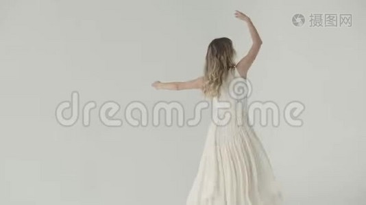 漂亮的女孩穿着白色的裙子在浅色的背景下跳舞。视频