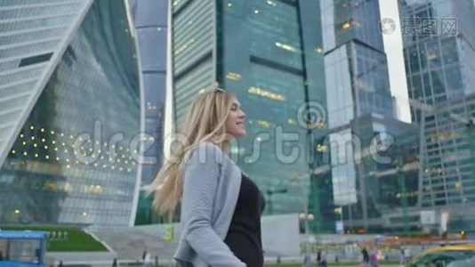 这个金发女孩在摩天大楼和城市高层建筑的背景下向相机发送一个空中吻。视频