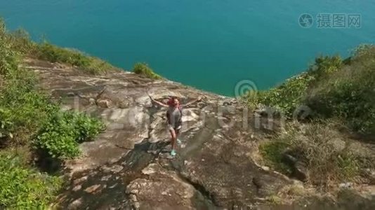 空中：年轻快乐的徒步旅行者女孩站在山岩上，张开双臂，微笑。 泰国Koh Phangan。视频