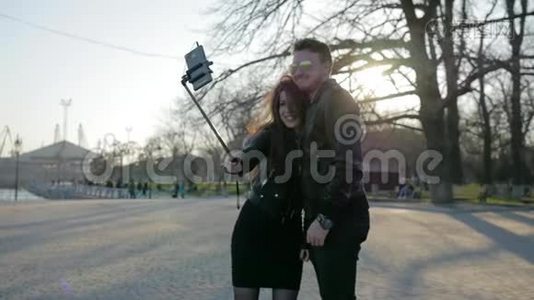 年轻情侣在背光，手机在自粘，网络交流，时尚男女孩在公园散步，视频