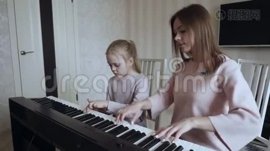 年轻的老师和小可爱的女孩在电动钢琴上演奏。视频