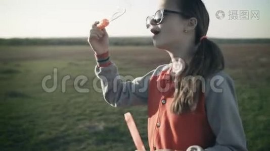 一个漂亮的年轻女孩在空旷的草地上吹肥皂泡。视频