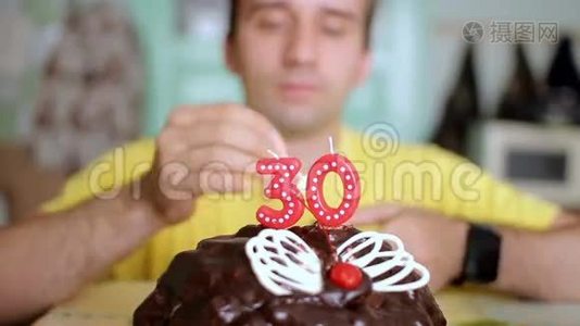 一个男人用蝴蝶翅膀在巧克力蛋糕上点燃30年的蜡烛。 这个人今天过生日。视频