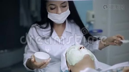 美容师在一个皮肤有问题的年轻女孩的脸上涂上一层面膜视频