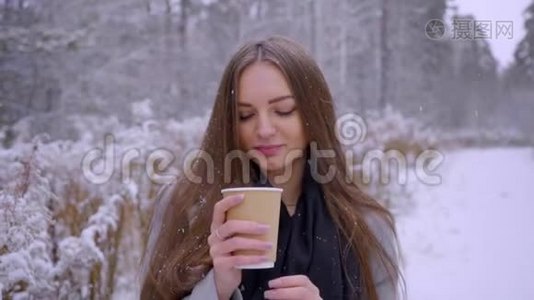 美丽的年轻女子，带着一次性咖啡杯，正在户外的冬季公园里喝茶或咖啡。 慢动作视频