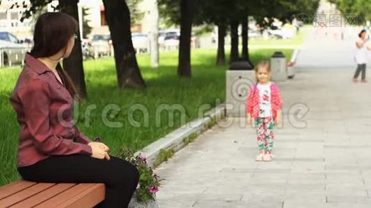 一个小女孩跑向坐在长凳上的母亲。视频