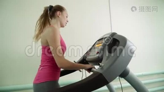 一个迷人的女孩正在健身房的跑步机上工作。视频