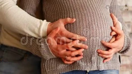 妈妈和爸爸手在怀孕的肚子上显示心脏的迹象。 怀孕夫妇抚摸怀孕的肚子。 准妈妈照顾视频