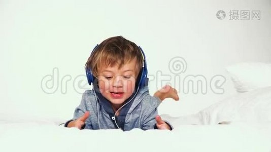 4岁男孩躺在床上，带着耳机玩平板电脑视频
