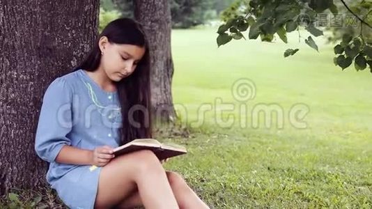 一个留着长发的漂亮小女孩读着一本书，坐在树下，梦见了一些令人愉快的事情视频