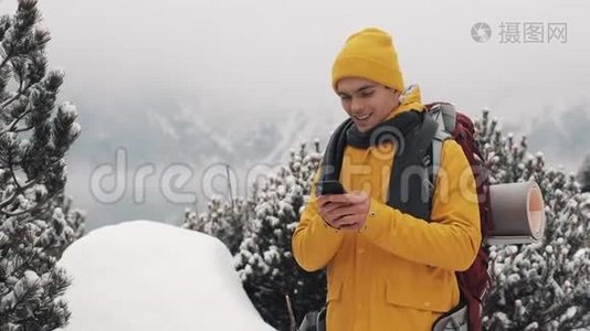 年轻的旅行者在徒步冬季旅行中使用智能手机。 白雪模糊的山角和湖。 旅行和视频