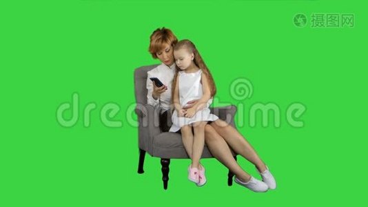 可爱的小女孩坐在妈妈的膝盖上，一边用绿色屏幕上的手机说话，Chroma键视频